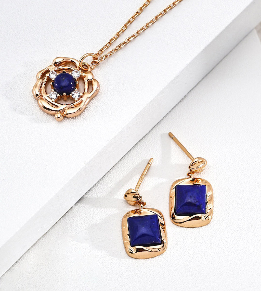 A gold jewelry set featuring a pendant necklace and matching drop earrings, both adorned with deep blue square and round lapis lazuli | BUCKLE Collective