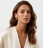 A woman with wavy brown hair models a gold necklace with a round turquoise pendant, along with matching drop earrings | BUCKLE Collective