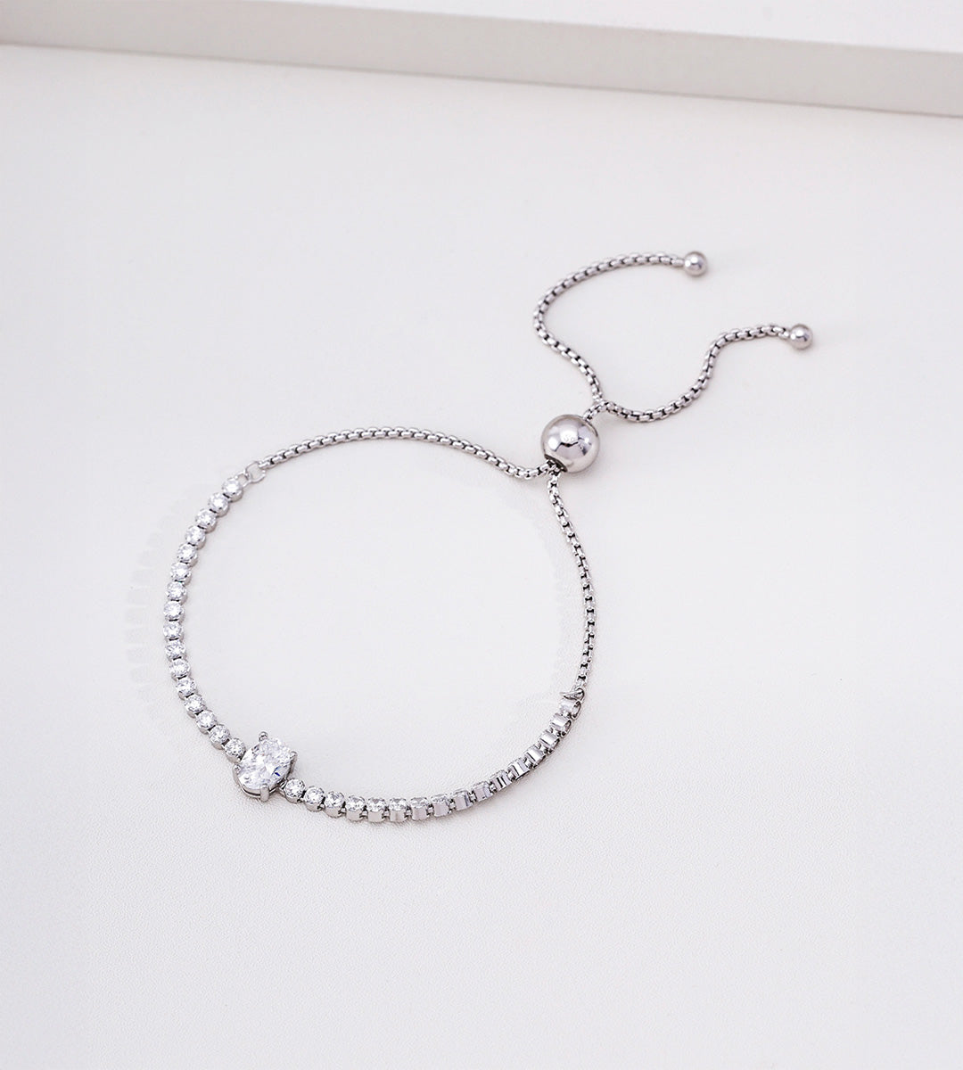 Silver-tone adjustable tennis bracelet with an oval cubic zirconia centre stone and twin chain ends with rounded tips.