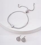Silver-tone oval cubic zirconia tennis bracelet on a white display, with a sliding ball closure and circular stud earrings below.


