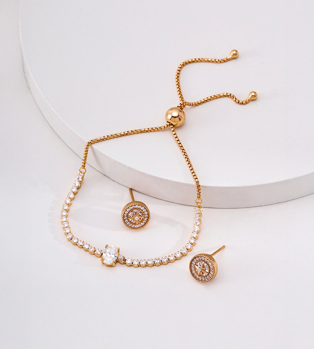 Gold-tone oval cubic zirconia slider bracelet draped over a white display beside circular halo-style stud earrings.