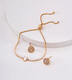 Gold-tone oval cubic zirconia slider bracelet draped over a white display beside circular halo-style stud earrings.