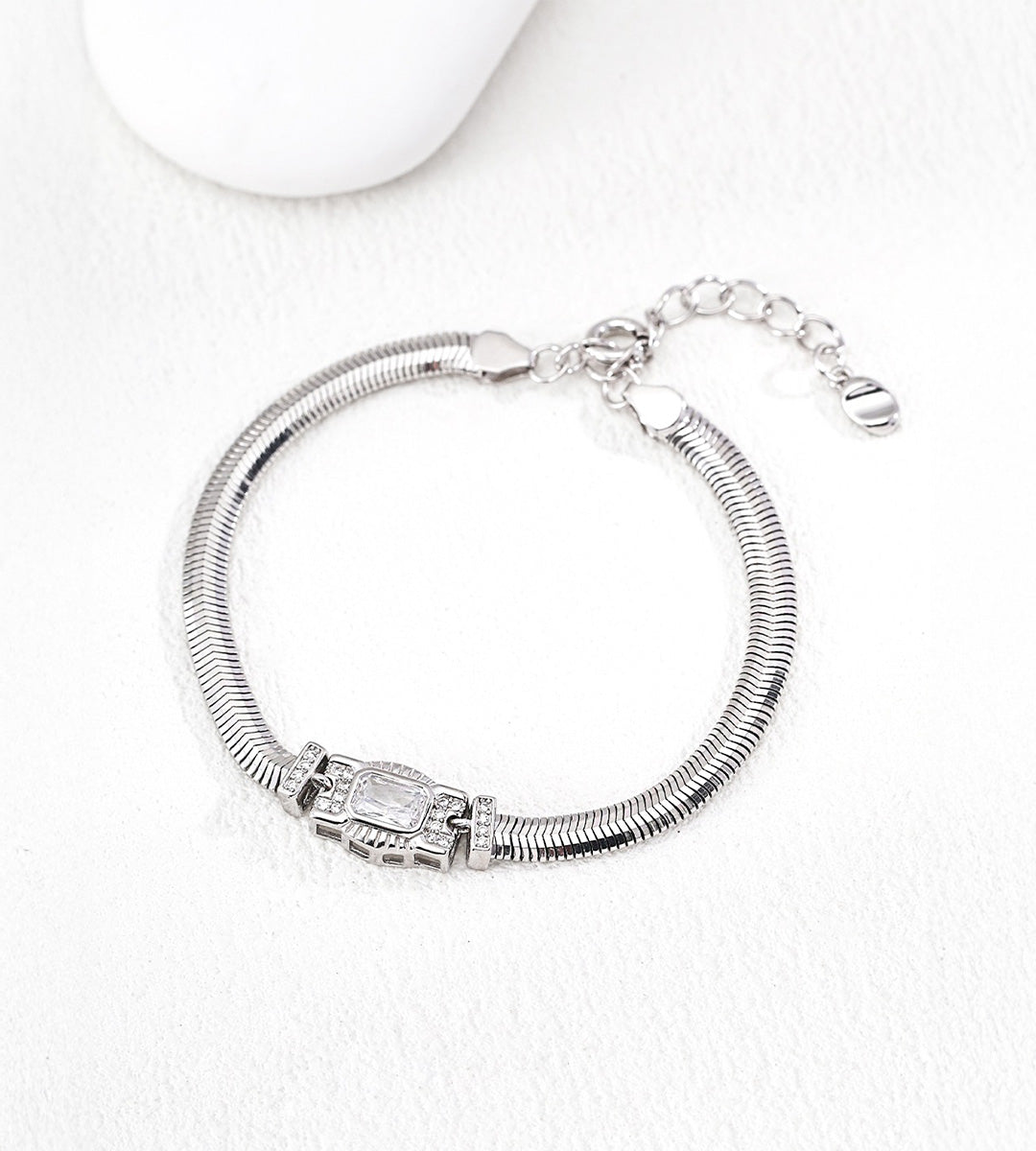 Silver-tone flat snake chain bracelet with a rectangular cubic zirconia centre and small side accents, showing its lobster clasp and extender.