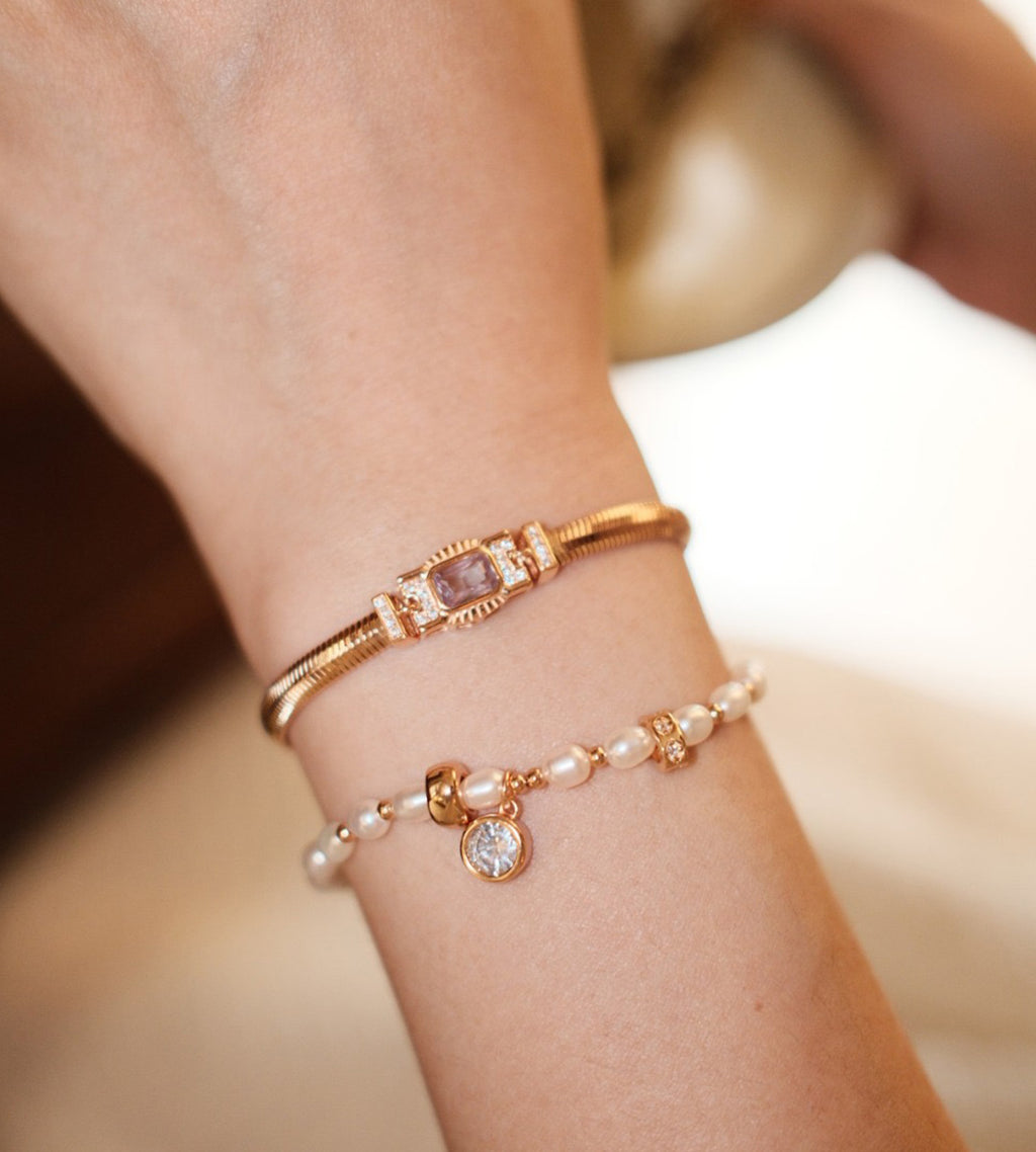 Vintage Gold rectangular cubic zirconia snake chain bracelet worn on the wrist, stacked with a pearl bracelet and round dangling charm.