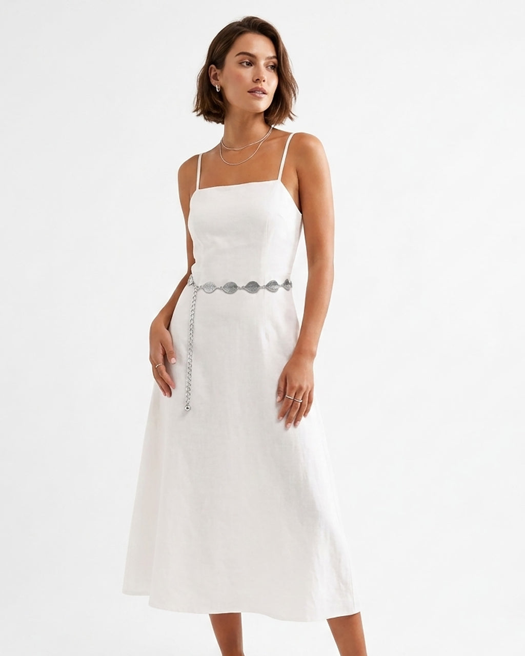 A woman modeling a white midi dress with thin straps, a square neckline, and a Bohemian silver leaf waist belt at the waist | BUCKLE Collective