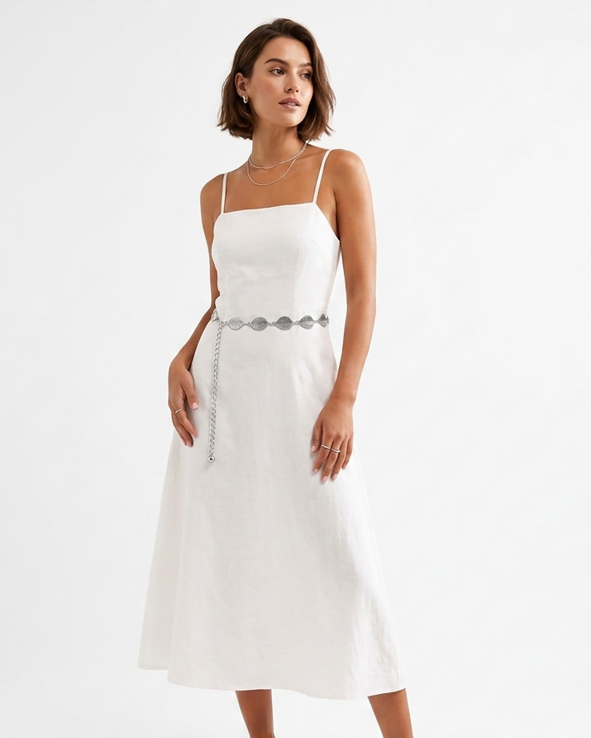 A woman modeling a white midi dress with thin straps, a square neckline, and a Bohemian silver leaf waist belt at the waist | BUCKLE Collective