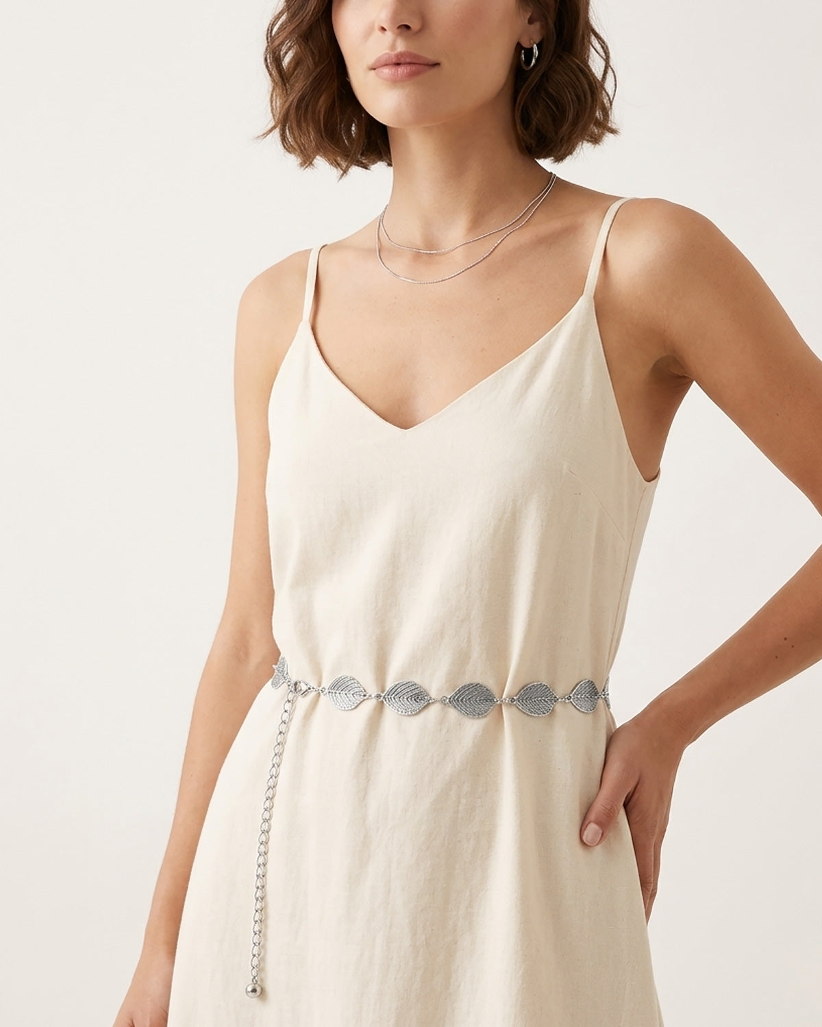 A woman wearing a cream-colored spaghetti-strap dress with a Bohemian silver leaf waist belt at the waist | BUCKLE Collective