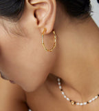 Close-up on a woman wearing 18K gold-plated S925 Silver bamboo hoop earrings and a delicate beaded necklace with white pearls and small black beads.