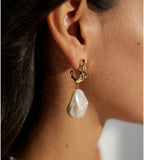 Side close-up of a worn baroque pearl drop earring, showing its irregular pearl and sculptural gold-plated top.