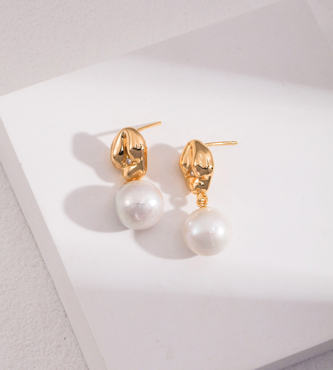 A pair of 18K gold-plated S925 silver drop earrings with a polished gold dumpling-shaped top accented with cirzonia and a dangling baroque white pearl