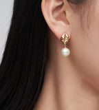 A close-up of a woman's ear wearing an 18K gold-plated drop earring with a dangling white pearl.