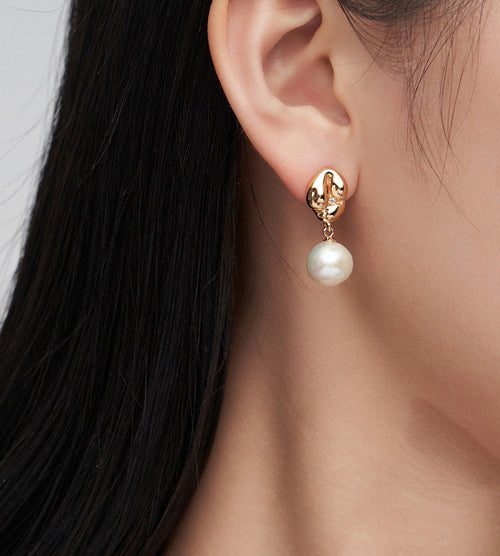A close-up of a woman's ear wearing an 18K gold-plated drop earring with a dangling white pearl.