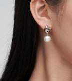 A close-up of a woman's ear wearing an 18K white-gold-plated drop earring with a dangling white pearl.