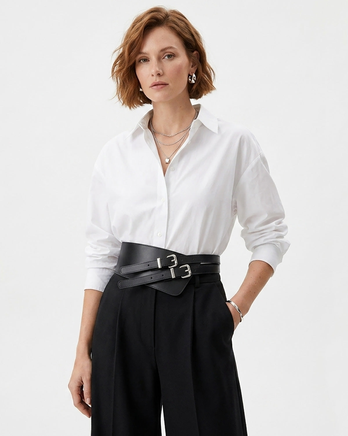 A woman wearing a white long-sleeve button-up shirt tucked into black high-waisted trousers with a wide statement black double-buckle belt by BUCKLE Collective