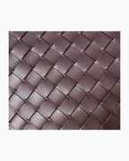 A close-up of a woven leather texture in a dark brown color, showing the detailed interlaced pattern of the material.