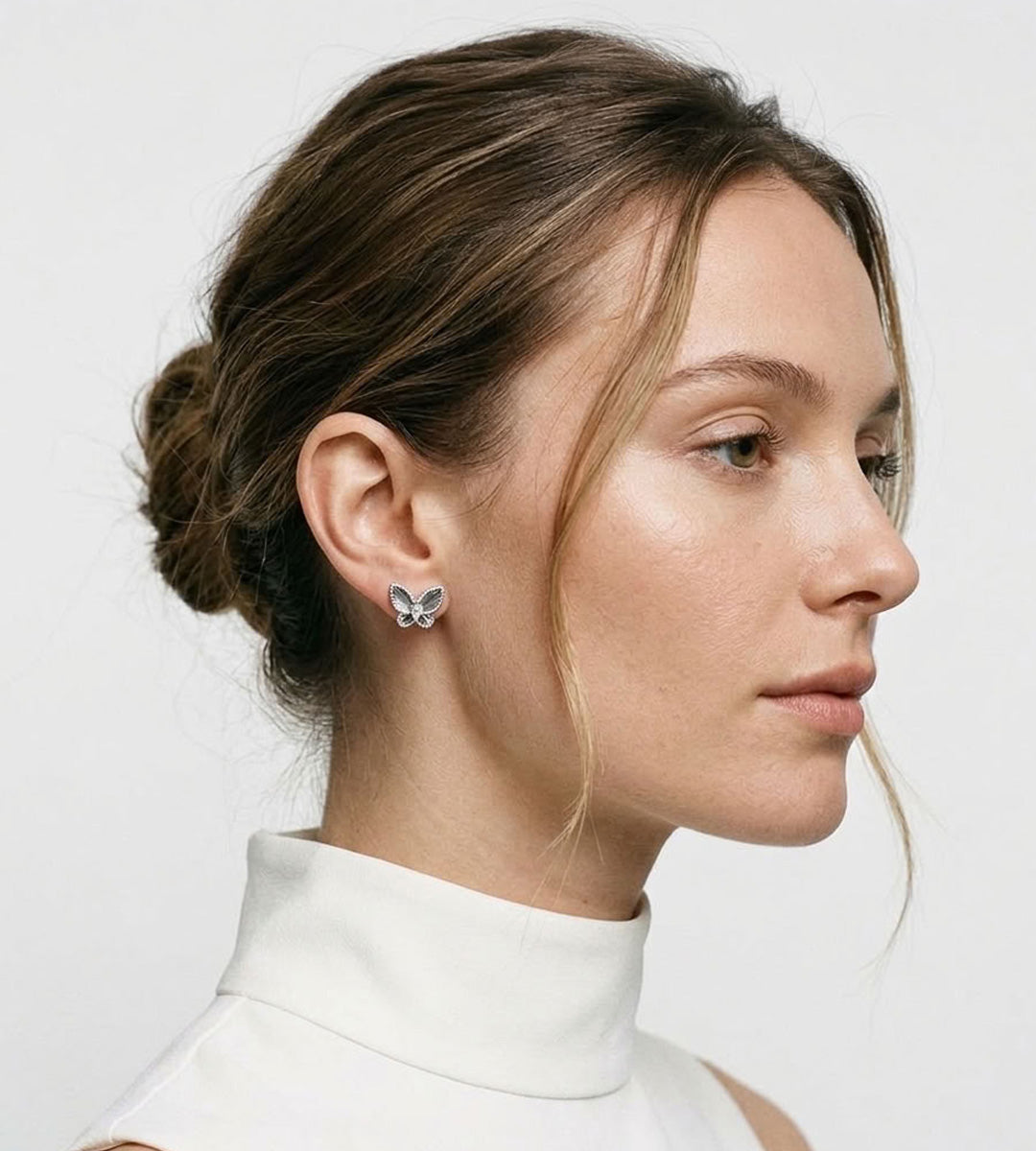 Model wearing a silver-tone butterfly stud earring with embossed wing details, styled with swept-back hair and a white top.