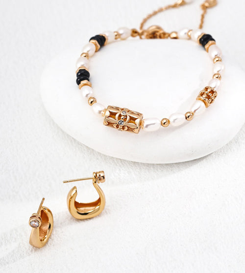 A gold and white beaded jewelry set featuring a bracelet and matching 18K gold-plated on S925 silver earrings, styled on a white stone and textured white surface.