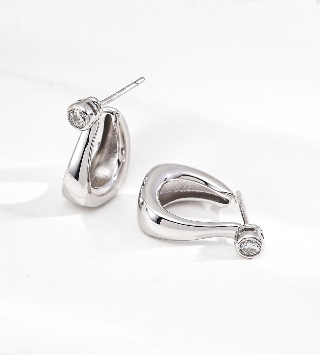 A pair of 18K gold-plated on S925 silver huggie hoop earrings with a clear round zirconia stone at the outer edge of each earring, displayed on a clean white background.