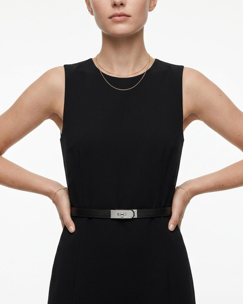 A model wearing a sleeveless black dress with a thin black saffiano leather belt with a silver-tone turn-lock buckle