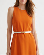 A woman wearing a sleeveless bright orange dress with a thin Classic White Saffiano Leather Belt with Gold Turn-Lock Buckle