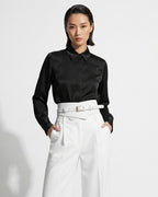 A model wearing a black satin long-sleeve button-down shirt tucked into high-waisted white trousers with a matching 2‑in‑1 White Women’s Leather Wide Transformable Statement Belt with Gold Buckle | BUCKLE Collective