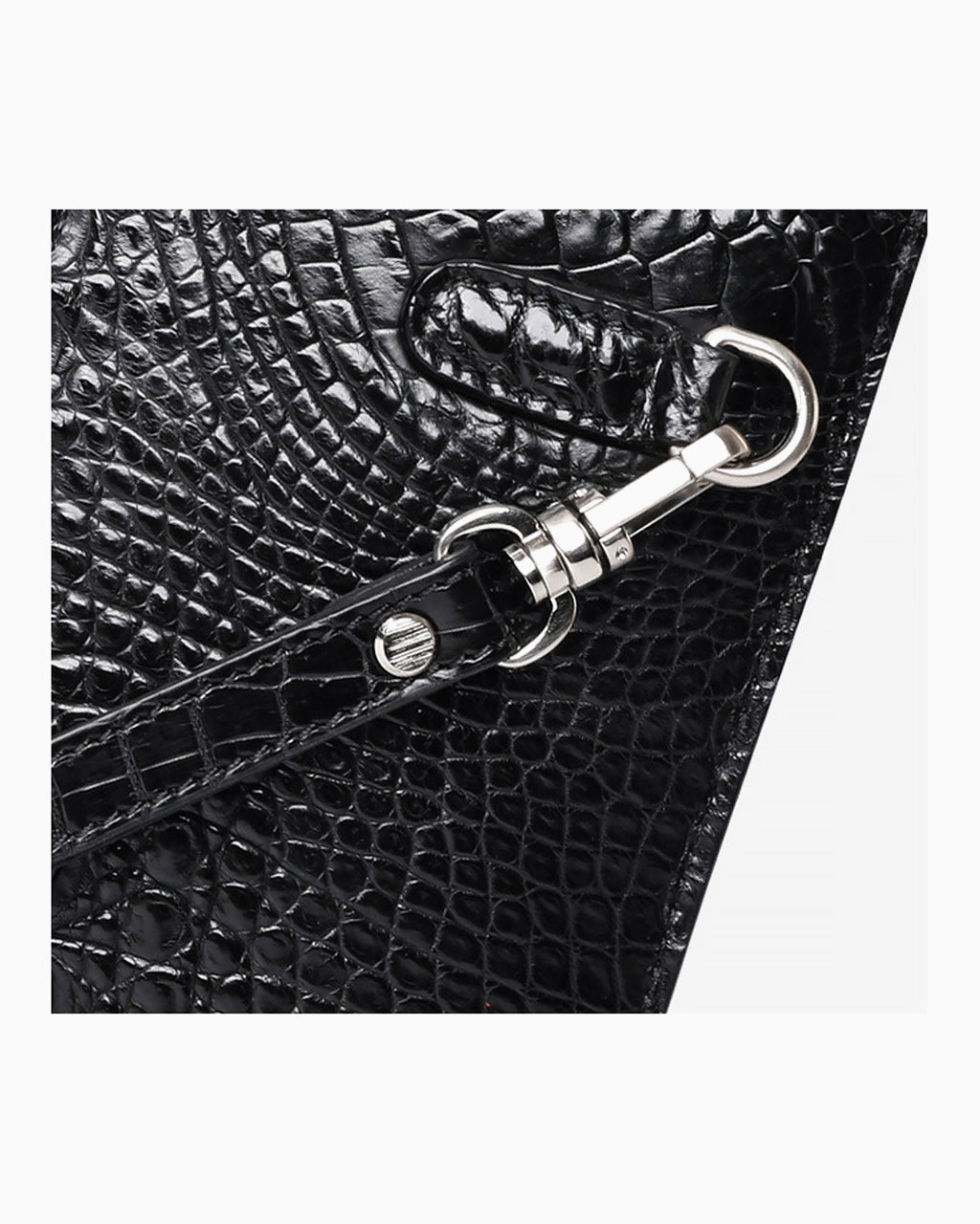 Close-up of a black crocodile leather clutch with a silver metal clasp and strap attachment on a light gray background | BUCKLE Collective