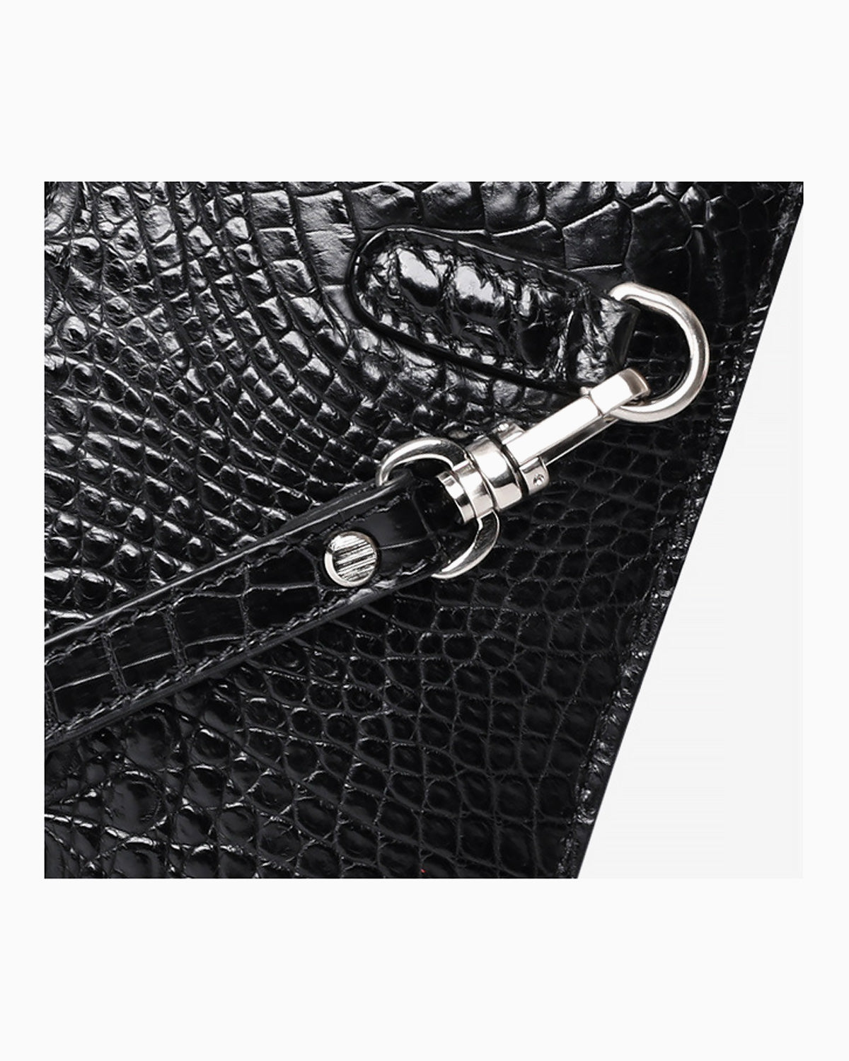 Close-up of a black crocodile leather clutch with a silver metal clasp and strap attachment on a light gray background | BUCKLE Collective