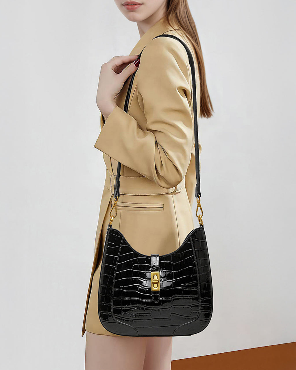 A woman in a stylish beige coat carries an Elegant Crocodile-Pattern Black Genuine Leather Shoulder Bag with Gold Hardware and crossbody strap
