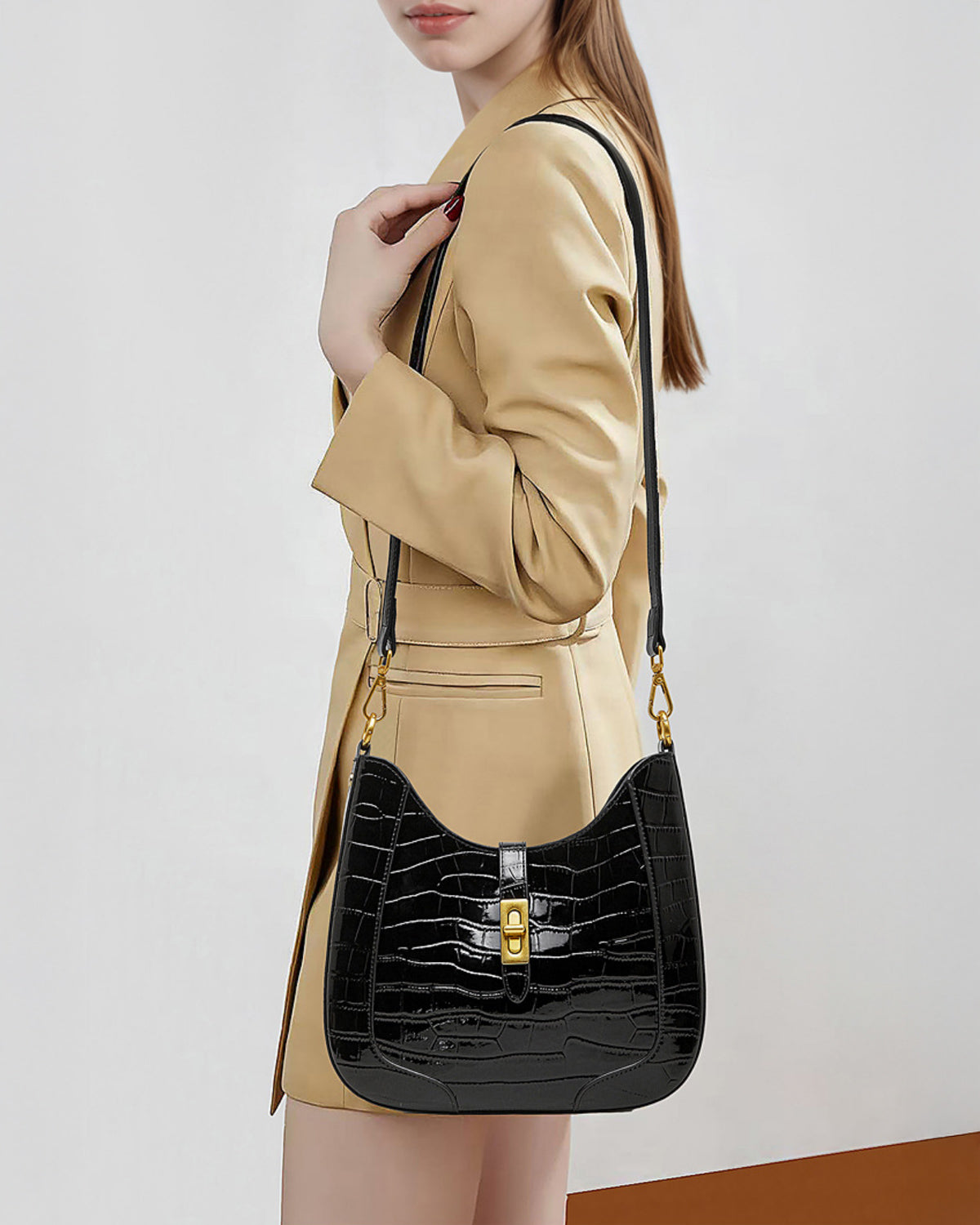 A woman in a stylish beige coat carries an Elegant Crocodile-Pattern Black Genuine Leather Shoulder Bag with Gold Hardware and crossbody strap