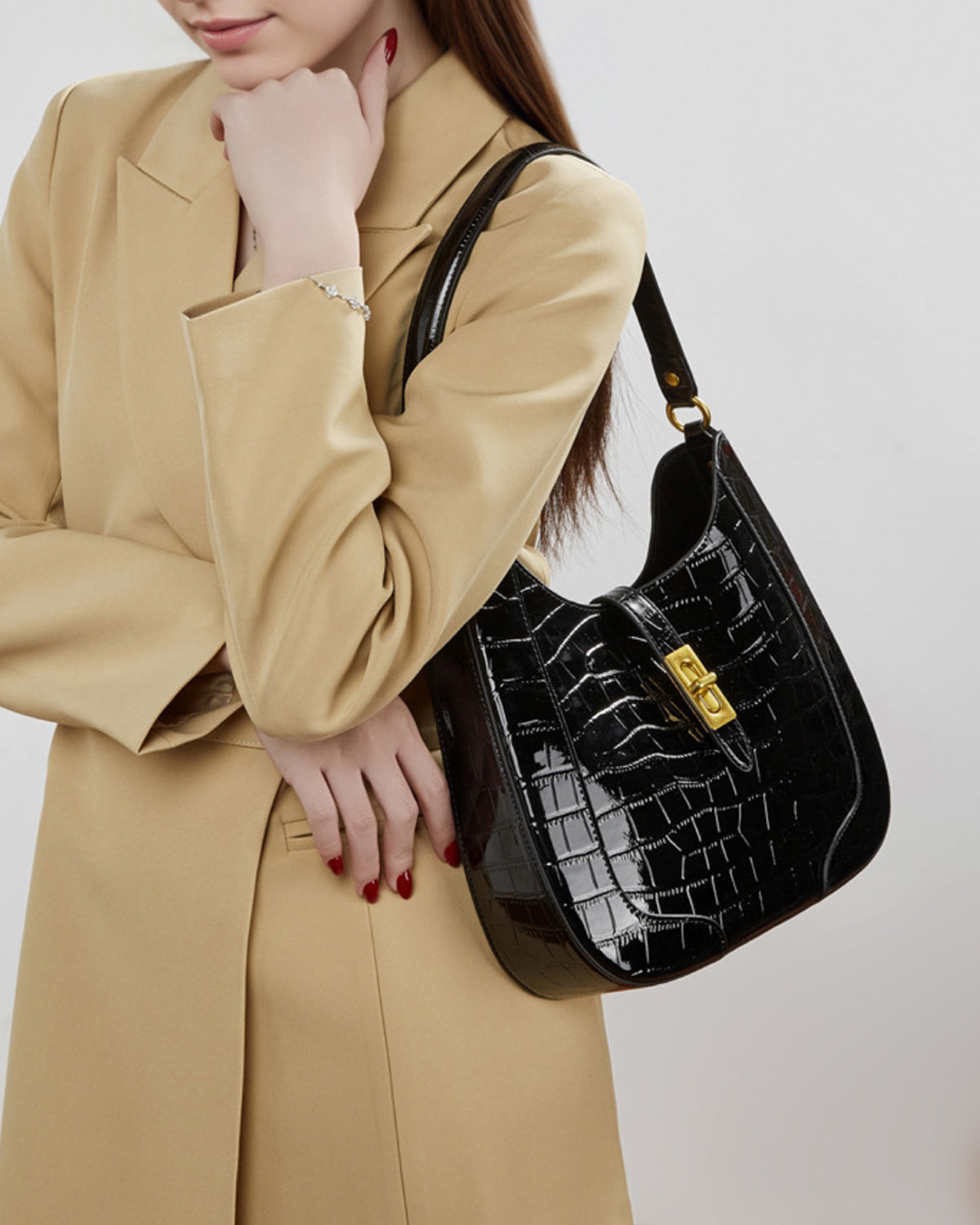 A woman in a stylish beige coat carries an Elegant Crocodile-Pattern Black Genuine Leather Shoulder Bag with Gold Hardware