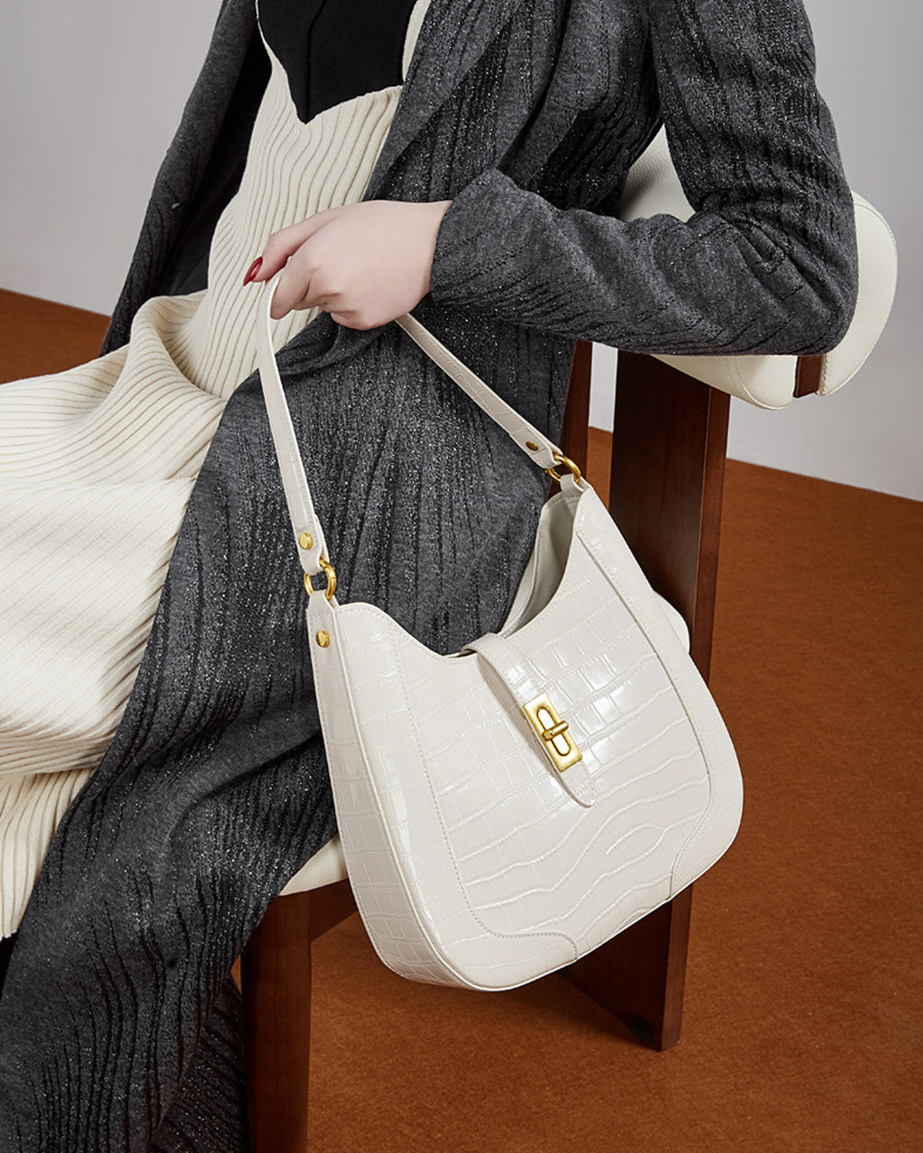Woman sitting on a chair with an Elegant Crocodile-Pattern White Genuine Leather Shoulder Bag with Gold Hardware