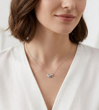 A close-up of a woman wearing a delicate 18K white-gold-plated S925 Silver Dainty Curved Bean Heart Necklace. She is wearing a white V-neck top | BUCKLE Collective