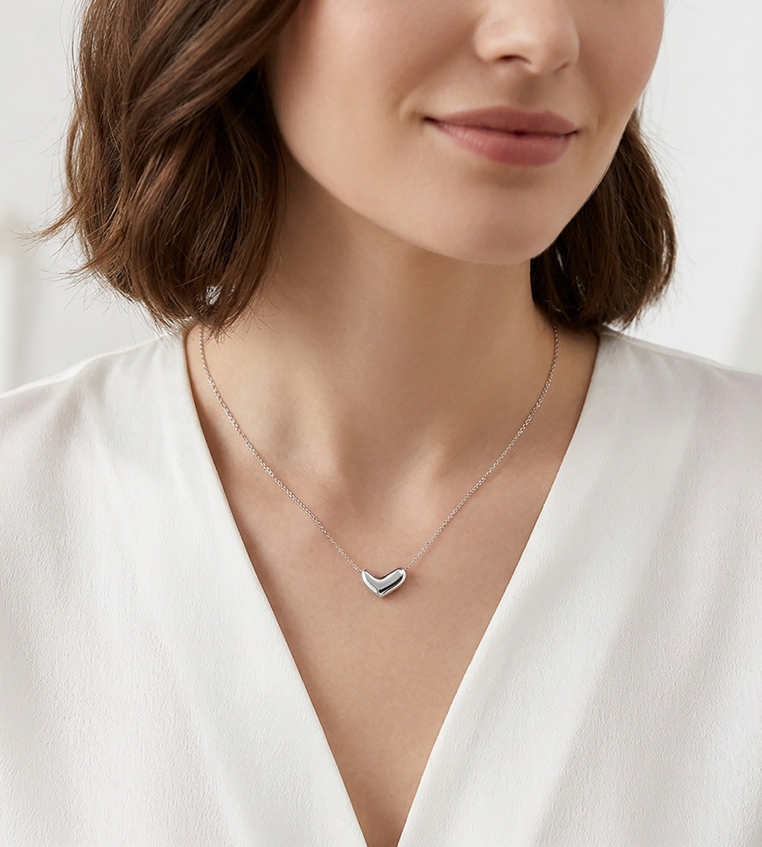 A close-up of a woman wearing a delicate 18K white-gold-plated S925 Silver Dainty Curved Bean Heart Necklace. She is wearing a white V-neck top | BUCKLE Collective