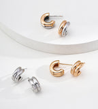 Three pairs of stacked hoop stud earrings, arranged on a clean white surface with a curved white pedestal.