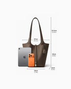 An extra-large Togo leather bucket tote bag shown on a light gray background with overlaid dimensions for width, height, and depth, plus a smartphone and tablet used as size references