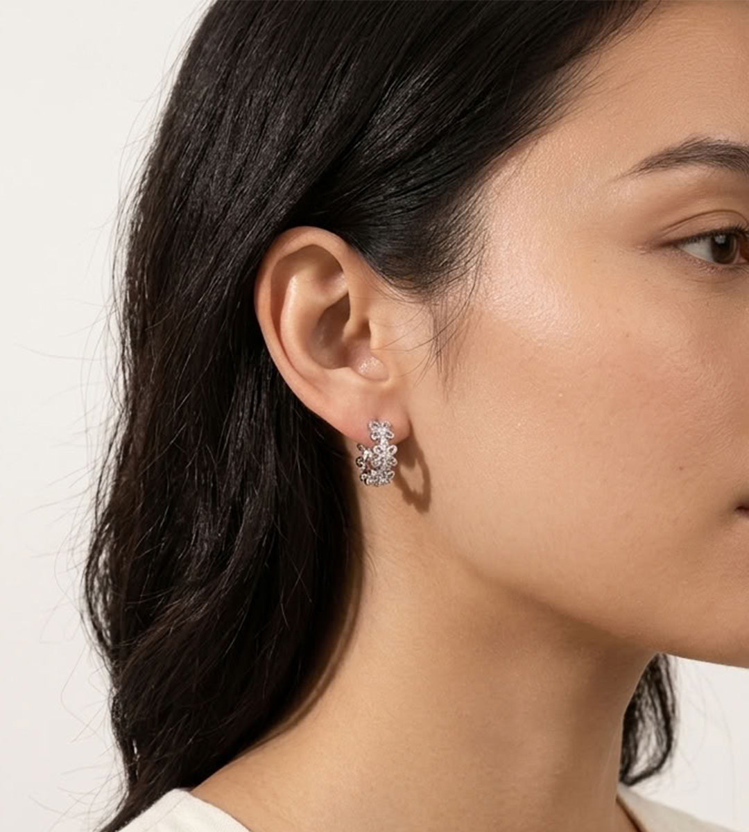 Model wearing a silver-tone floral huggie hoop earring with hollow-carved four-petal flowers and cubic zirconia accents.

