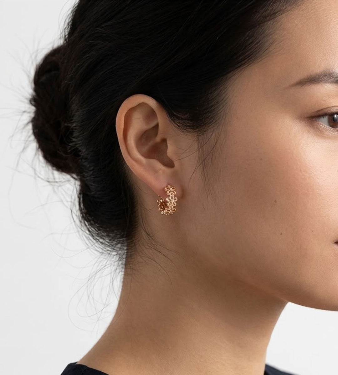 Model wearing an 18K gold-plated floral huggie hoop earring with hollow-carved four-petal flowers and cubic zirconia accents.