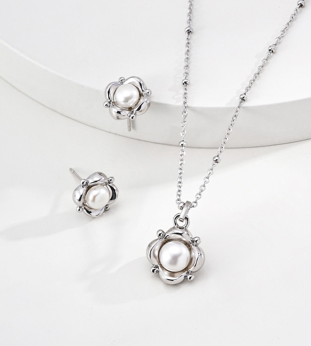 18K white-gold-plated jewelry set featuring a flower-shaped pendant necklace with a white pearl and matching stud earrings, displayed on a clean white background.