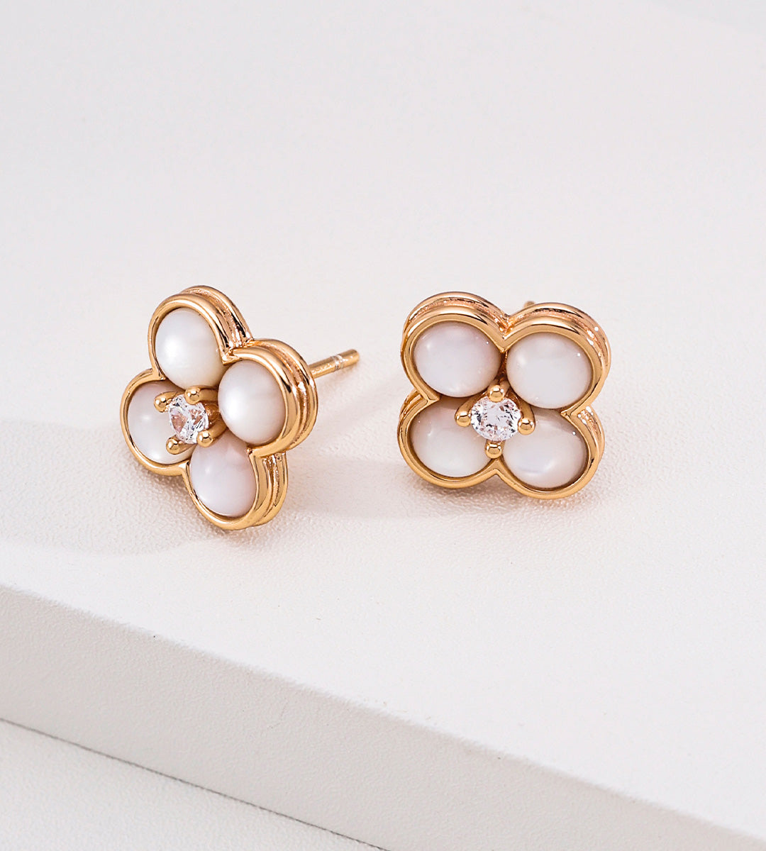 A pair of 18K gold-plated S925 silver four-petal flower stud earrings with white mother-of-pearl inlays and a small cubic zirconia at the center, displayed on a clean white surface.
