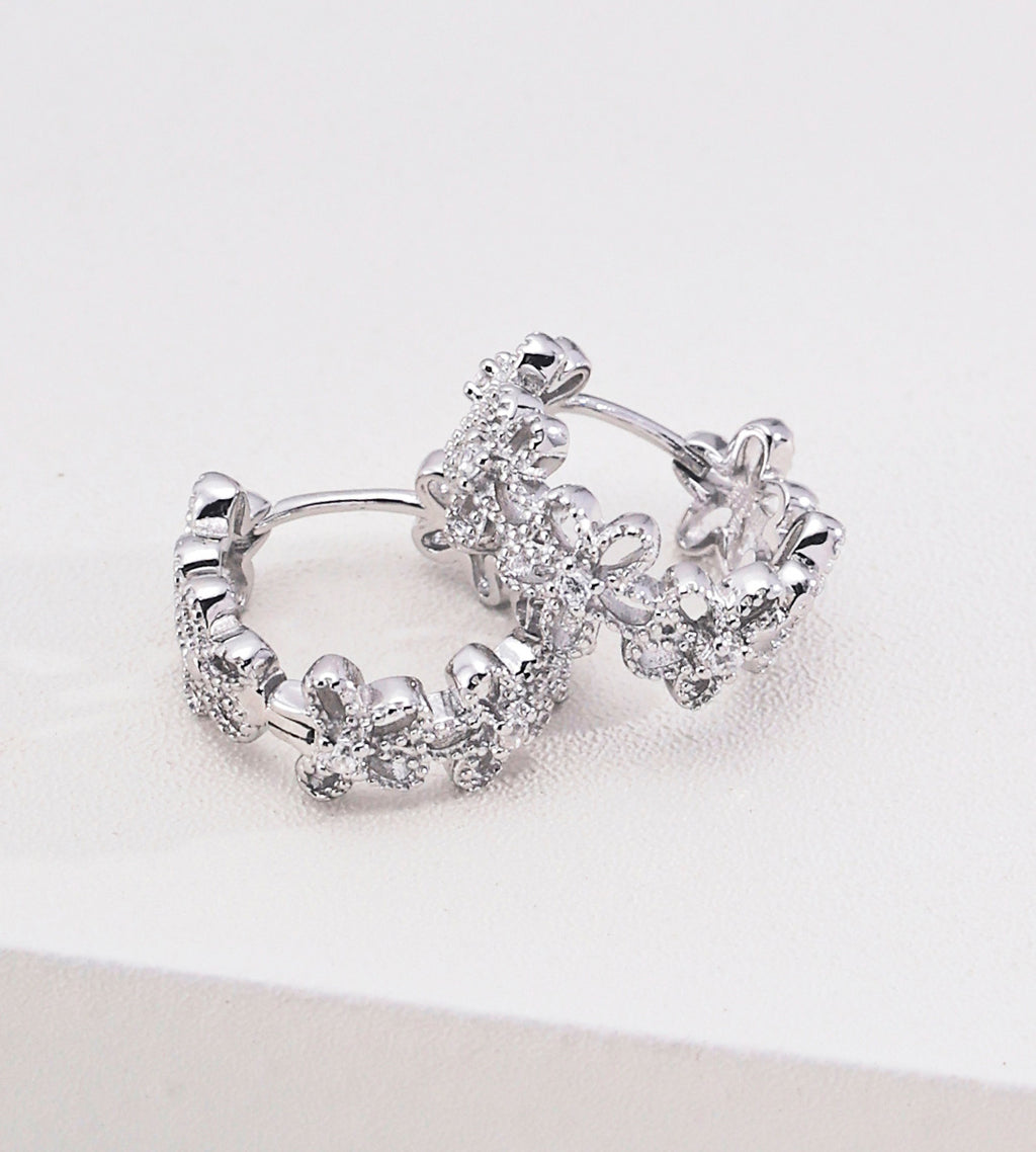 Floral hollow-carved huggie hoop earrings in 18K white gold plating — continuous CZ flower band, openwork floral silhouette, S925 sterling silver, BUCKLE Collective
