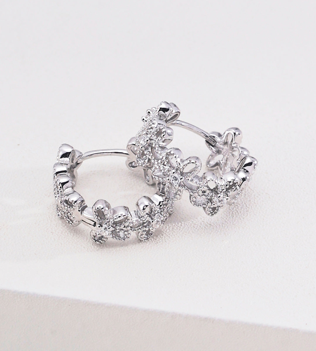 Floral hollow-carved huggie hoop earrings in 18K white gold plating — continuous CZ flower band, openwork floral silhouette, S925 sterling silver, BUCKLE Collective