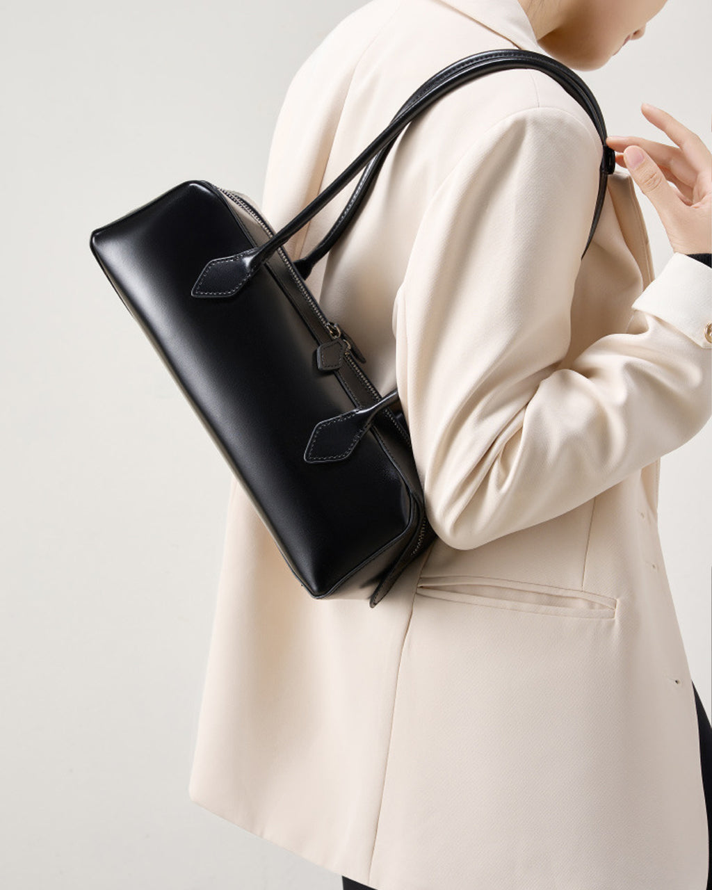 Woman in a stylish white jacket wearing a black Leather Baguette Handbag