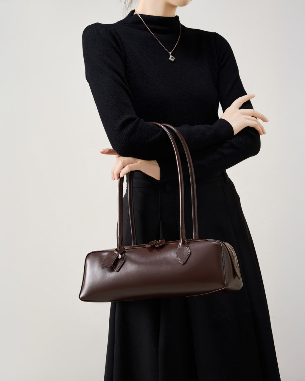 Woman in an elegant black outfit with a leather baguette handbag in brown color