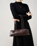 Woman in an elegant black outfit with a leather baguette handbag in brown color