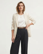 A woman modeling a light beige blazer over a white top and dark charcoal wide-leg trousers, styled with a slim brown classic belt