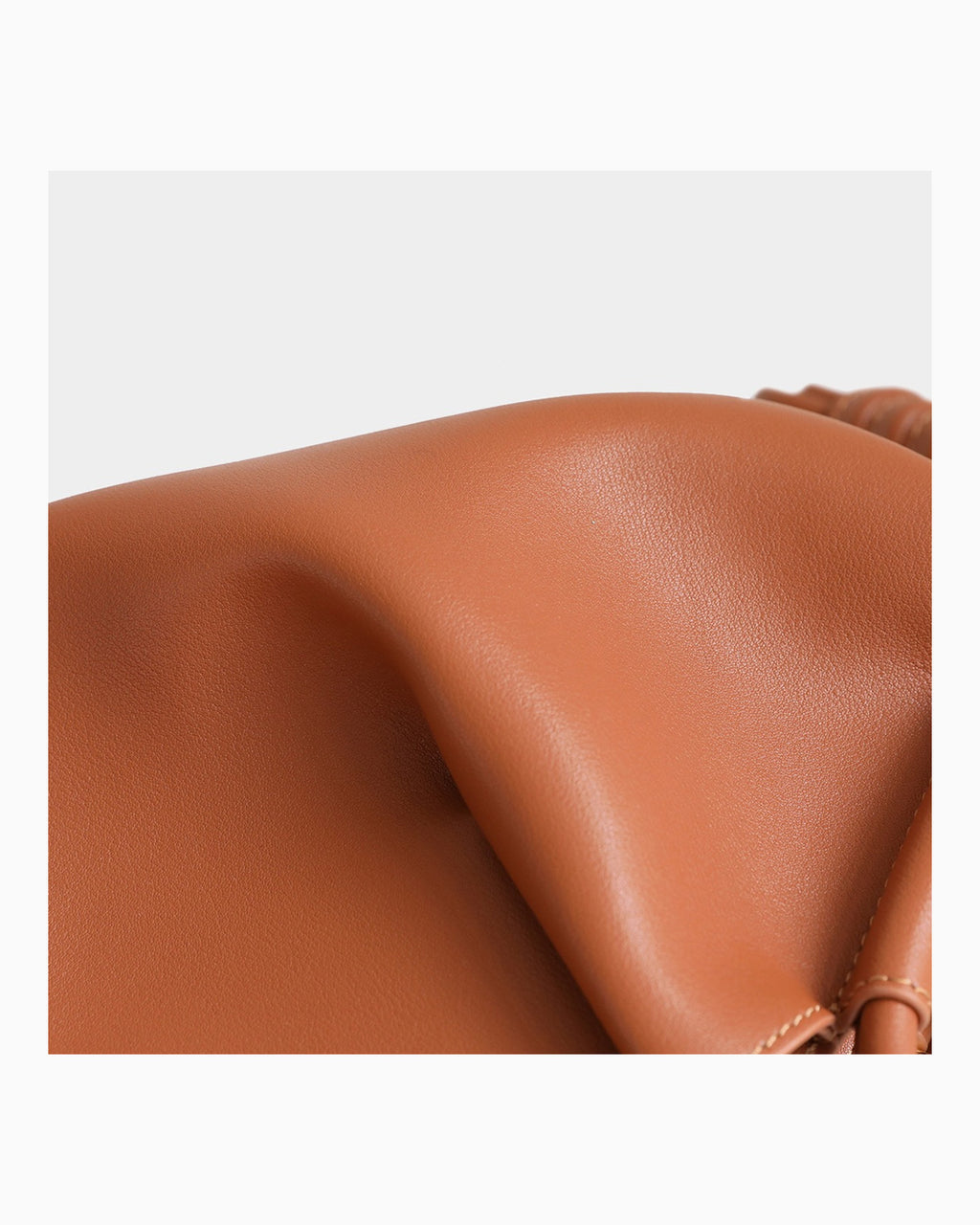 Close-up of a smooth, warm tan-brown leather surface with soft folds and a small portion of a matching strap or loop visible on the right side