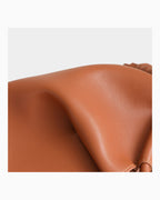 Close-up of a smooth, warm tan-brown leather surface with soft folds and a small portion of a matching strap or loop visible on the right side
