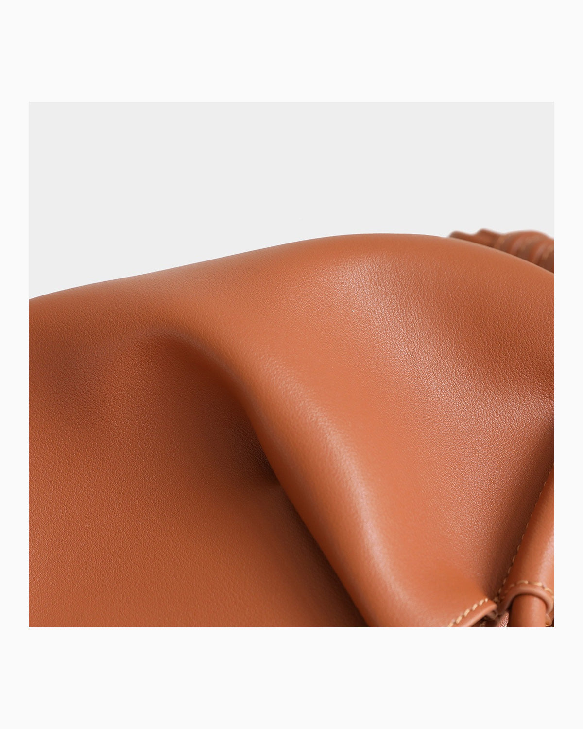 Close-up of a smooth, warm tan-brown leather surface with soft folds and a small portion of a matching strap or loop visible on the right side