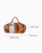 Dumpling Handbag with Knotted Strap shown on a light gray background with overlaid dimension lines and measurements indicating width, height, and depth, plus a smartphone used for scale.