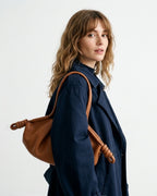 A woman wearing a navy blue jacket and carrying a brown leather shoulder bag with knotted strap details | BUCKLE Collective
